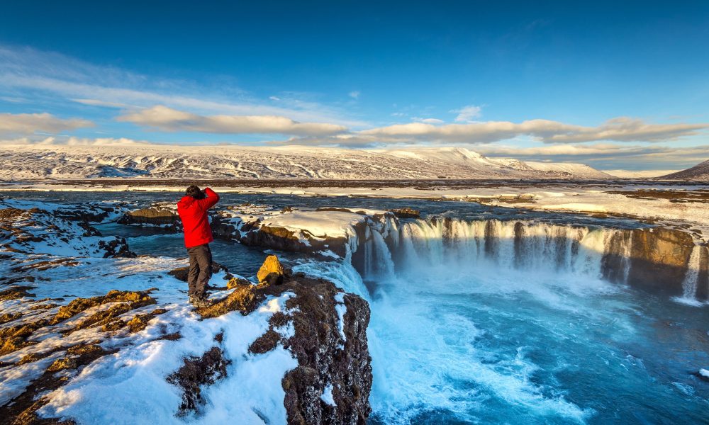 Photoghaper taking a photo at Godafoss waterfall in winter, Iceland.